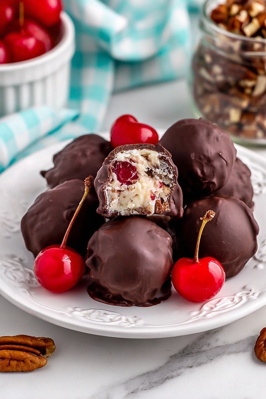A white plate with decorative cut edges holds a pile of round chocolate balls, each coated in smooth dark chocolate. One ball is broken open on top, showing a creamy white filling mixed with small bits of nuts and a bright red cherry piece in the middle. Garnishing the plate are three whole bright red cherries with stems. The plate sits on a white marbled surface with a light blue and white checkered cloth and a jar of pecans nearby in the background. Photo taken with an iphone --ar 2:3 --v 7