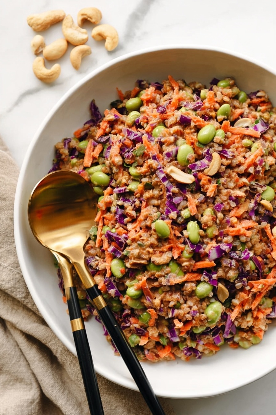 A white bowl filled with a colorful salad made of many layers: small brown grains, green edamame beans, orange shredded carrots, small purple cabbage pieces, and beans mixed evenly together. The salad has a slightly moist texture, showing a creamy or peanut-like dressing holding the ingredients. Near the bowl, two black chopsticks with gold ends and a large gold spoon rest on the edge, pointing inward. In the background on the left side, a few whole cashew nuts lay on the white marbled surface. The photo taken with an iphone --ar 2:3 --v 7