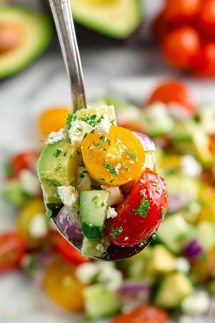 A close-up view of a spoonful of salad showing three main layers: the bottom layer has bright red and yellow cherry tomatoes, the middle layer contains light green avocado chunks mixed with small pieces of red onion, and the top layer is sprinkled with fresh green herbs and small white cheese crumbles. The salad in the background fills a white bowl and rests on a white marbled surface, with more tomatoes and a halved avocado blurred in the back. Photo taken with an iphone --ar 2:3 --v 7