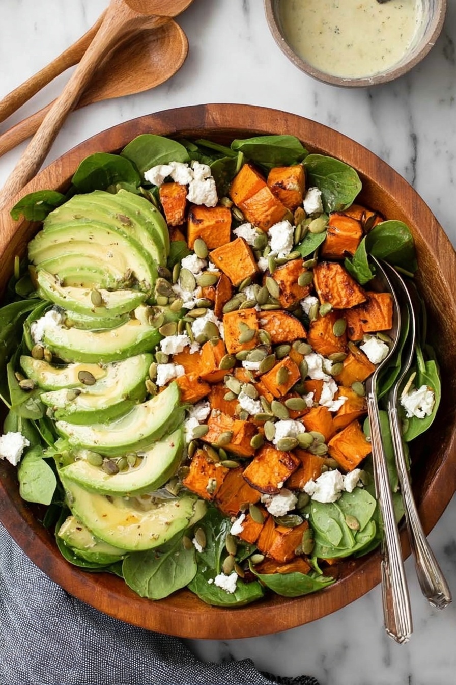 A wooden bowl filled with a salad made of several layers: the bottom layer is fresh green spinach leaves, followed by thick slices of light green avocado placed evenly on top. Scattered over the avocado are bright orange roasted sweet potato chunks with slightly charred edges. White crumbled cheese is sprinkled across the salad, and small green pumpkin seeds are spread evenly over the top. There are two silver spoons resting on the right side inside the bowl, and a small bowl with creamy dressing and a wooden spoon is in the upper right corner on a white marbled surface with a gray cloth on the bottom left. Photo taken with an iphone --ar 2:3 --v 7