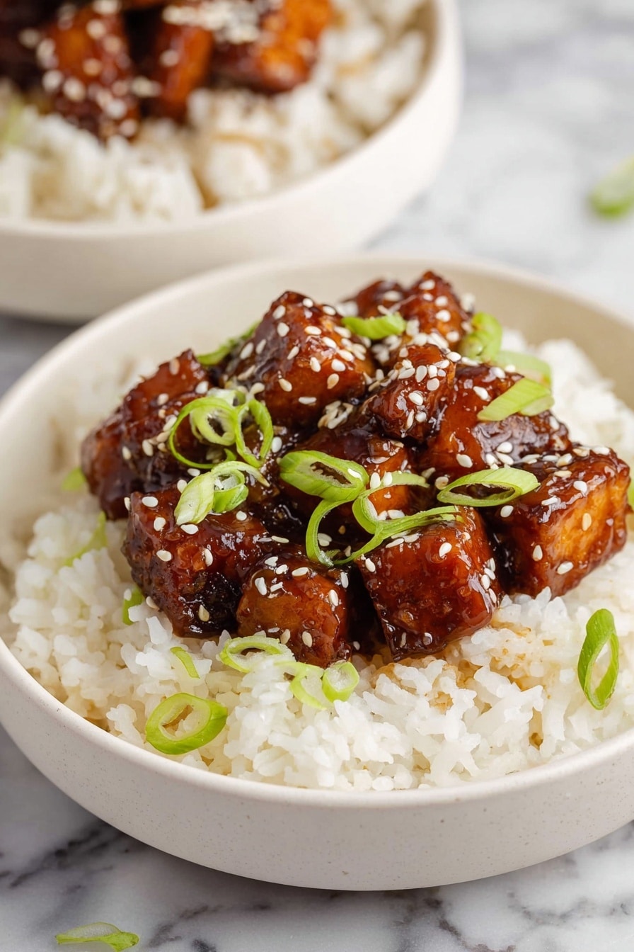 orange tofu - A white bowl filled with a base layer of fluffy white rice, with a thick layer of glossy, dark brown glazed tofu cubes placed in the center on top. The tofu pieces are sprinkled with white sesame seeds and decorated with thinly sliced green spring onions scattered across both the tofu and the rice. The bowl sits on a white marbled surface with another similar bowl blurred in the background. Photo taken with an iphone --ar 2:3 --v 7