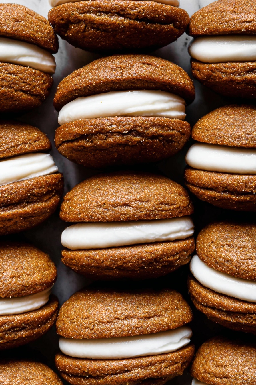 The image shows a close-up view of nine sandwich cookies stacked closely together in three rows and three columns. Each cookie has two soft, round layers with a rough texture and warm brown color, like gingerbread or molasses. Between each pair of cookie layers, there is a thick middle layer of creamy white filling that is smooth and slightly shiny. The white cream is evenly spread and slightly visible from the sides, making a clear contrast with the dark cookies. The background is a white marbled texture, emphasizing the warm colors of the cookies. photo taken with an iphone --ar 2:3 --v 7