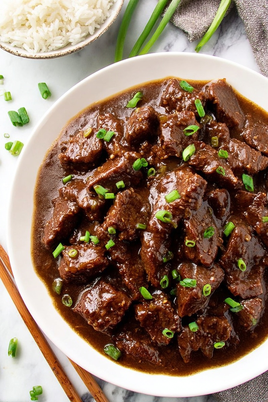 The image shows a white plate filled with dark brown beef strips covered in a thick, shiny sauce. The beef pieces are soaked in the sauce and appear tender and moist. Small pieces of bright green chopped spring onions are sprinkled evenly over the beef, adding a pop of color. The plate is placed on a white marbled surface. In the top left corner, a partial view of a white bowl filled with white rice is visible, with brown wooden chopsticks resting on the bowl. Photo taken with an iphone --ar 2:3 --v 7