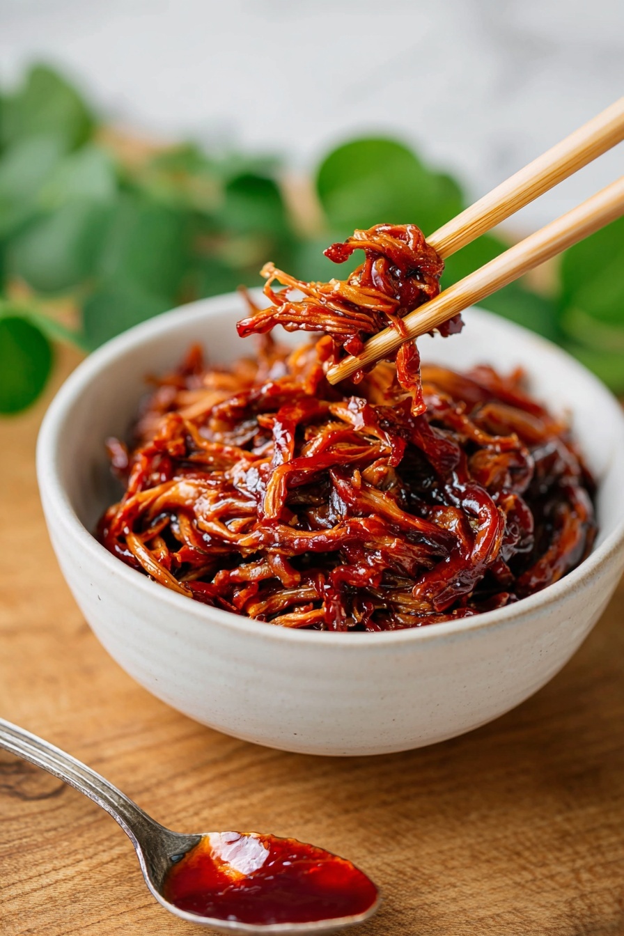 A white bowl sits on a wooden surface with a layer of white steamed rice filling most of the bowl. On top, there is a rich, glossy layer of shredded dark brown meat coated with a sticky sauce, giving it a shiny, wet look. The meat is sprinkled with small pieces of bright green chopped herbs evenly spread over the top. In the background, a faint white marbled texture is visible with some green leaves blurred softly. A gray cloth is partially shown near the bowl. Photo taken with an iphone --ar 2:3 --v 7