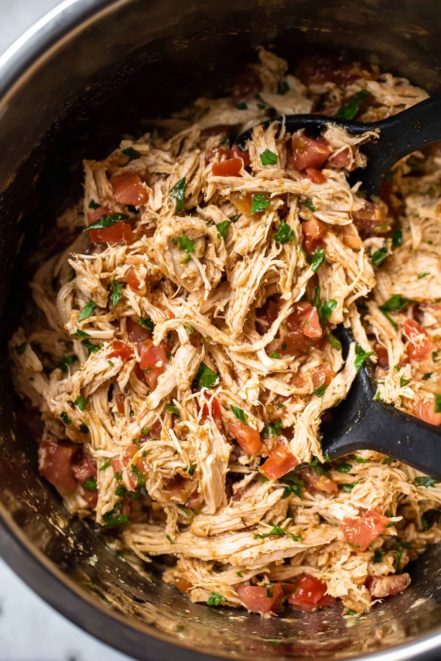 The image shows a close-up of shredded chicken mixed with small bits of red tomatoes and green herbs, all inside a shiny stainless steel pot. The shredded chicken is light brown with a soft, stringy texture, spread evenly throughout the pot. Scattered pieces of bright red tomato add color contrast, while small green herb leaves are spread throughout, adding freshness. Black serving spoons are placed inside the pot, partly submerged in the chicken mixture. The shiny surface inside the pot reflects the colors of the ingredients. The background is a white marbled texture. photo taken with an iphone --ar 2:3 --v 7