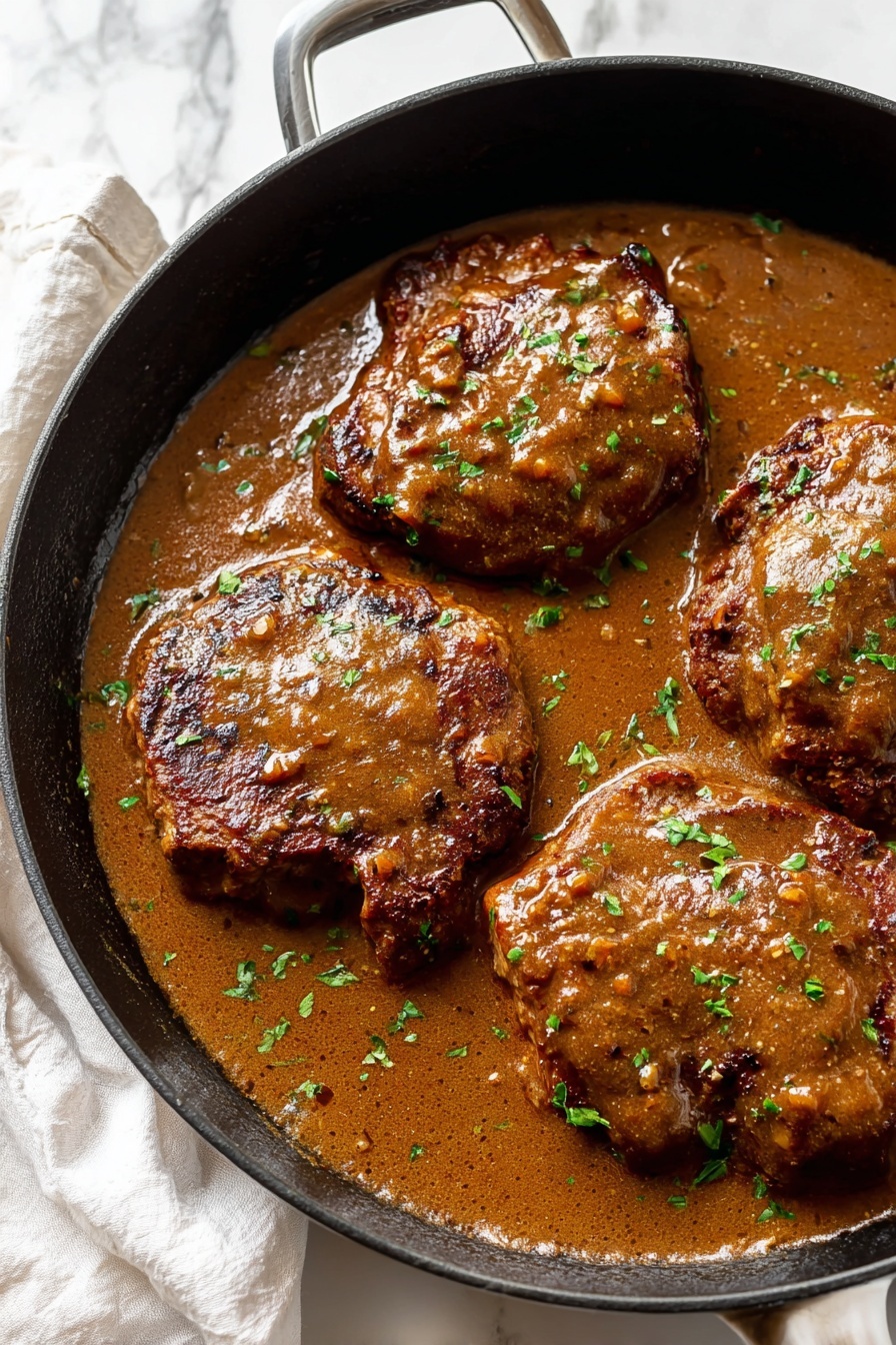 The image shows a black skillet filled with four cooked meat pieces covered in a thick brown sauce. The meat pieces have a slightly crispy texture with browned edges and are partially submerged in the rich sauce that has a smooth but textured appearance. Small green herb bits are sprinkled over the meat and sauce, adding contrast. The skillet is placed on a white marbled surface with a white cloth napkin nearby. Photo taken with an iphone --ar 2:3 --v 7