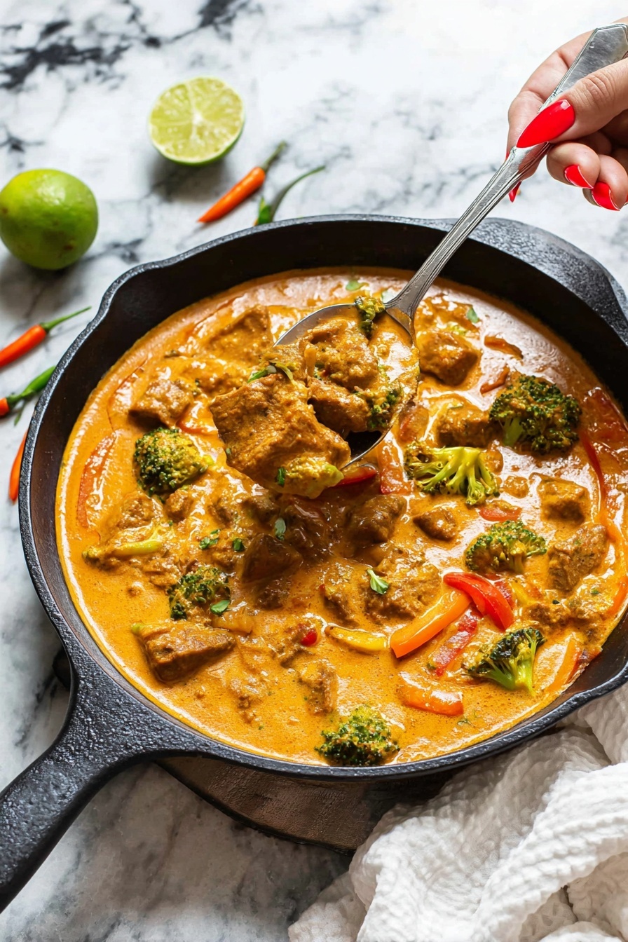 A black cast iron skillet holds a creamy orange curry filled with chunky pieces of meat, small green broccoli florets, and red bell pepper slices. The sauce is thick and smooth, covering the ingredients well. Woman’s hand with red nail polish holds a silver spoon lifting a scoop of the curry, showing the rich texture. The skillet rests on a white marbled surface with a white cloth and a whole lime behind it. Three small chili peppers in red, orange, and green lie beside the skillet. photo taken with an iphone --ar 2:3 --v 7