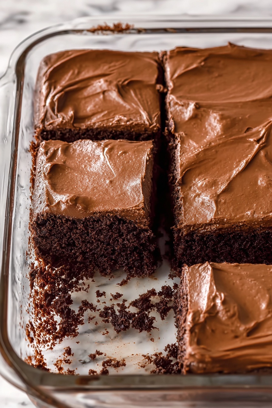 The image shows a clear glass baking pan with a thick, dark brown chocolate cake inside. The cake has a smooth, shiny layer of light brown chocolate frosting spread evenly on top. Three square pieces are cut from the cake and are lying next to the cake inside the pan, showing the dense, moist texture of the dark cake beneath the frosting. The background has a white marbled texture. photo taken with an iphone --ar 2:3 --v 7