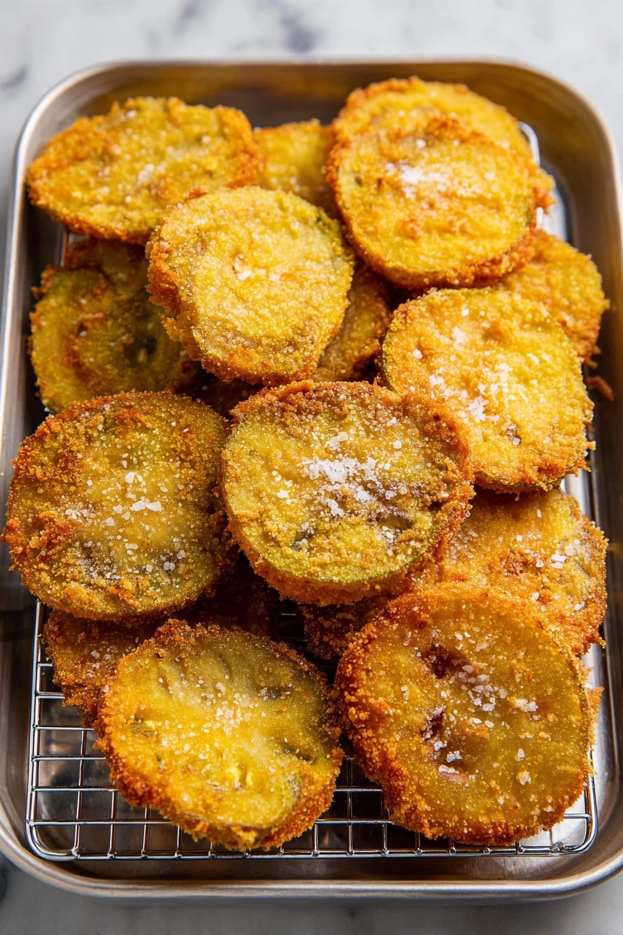 A silver metal tray with a silver wire rack inside holds about 14 round, golden brown fried slices arranged closely together with some overlapping. Each slice shows a rough, crispy texture with tiny bumps and is sprinkled lightly with flakes of coarse salt. The golden color varies slightly from slice to slice, with edges darker and more textured. The background is a white marbled surface. photo taken with an iphone --ar 2:3 --v 7