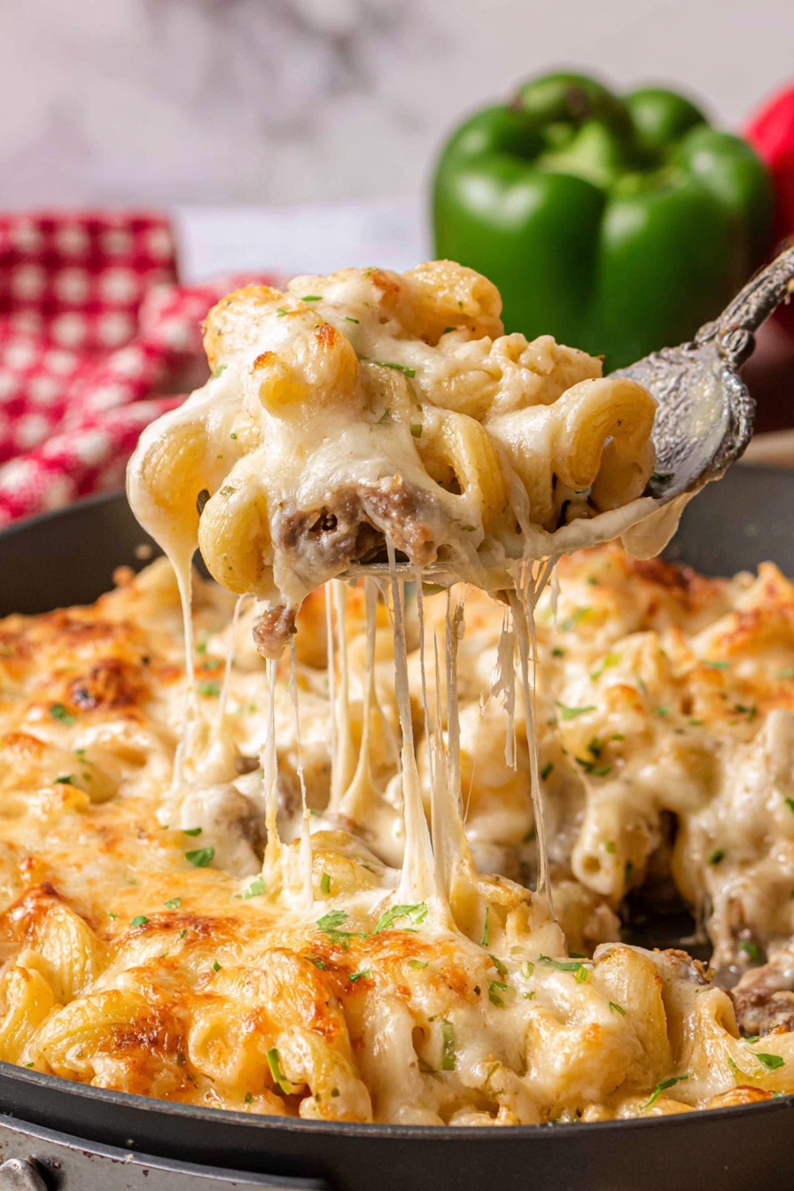 A top-down view of a round black pan filled with macaroni pasta mixed with pieces of cooked meat in a creamy sauce. On top of the pasta, there are seven large, round white cheese slices evenly placed to cover most of the surface. The pan is on a gray stone surface with a small wooden board holding a white container of pink salt and a small black bowl of mixed peppercorns, along with a bulb of garlic and a whole onion nearby. A red and white checkered cloth is partially folded on the right side. Photo taken with an iphone --ar 2:3 --v 7